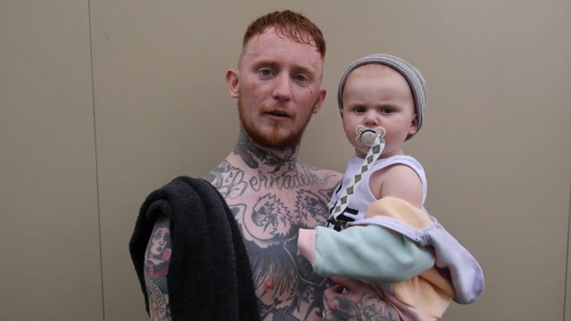 Band frontman holds baby as they book look to the camera in disbelief